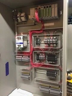 Open electrical control cabinet with wiring, relays, terminal blocks, and red cable conduit inside.