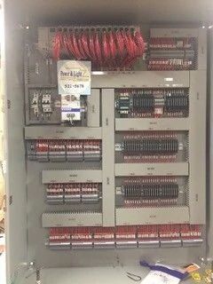 Electrical control panel with rows of red wiring and circuit breakers inside a metal cabinet.