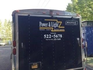 Black utility trailer with Power & Light Z signage and phone number 522-5678 parked outdoors