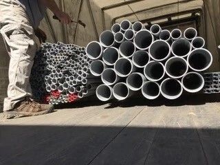 Worker beside stacked gray plastic pipes inside a truck trailer