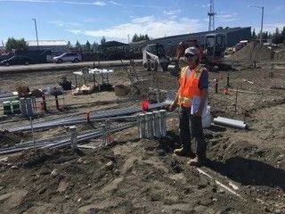 Construction worker in orange safety vest standing beside pipes at an outdoor worksite