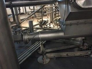 Industrial machinery and metal pipes in a factory interior, with a large black pipe assembly in the foreground
