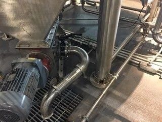 Industrial motor and stainless steel piping beside a grated floor drain in a factory setting