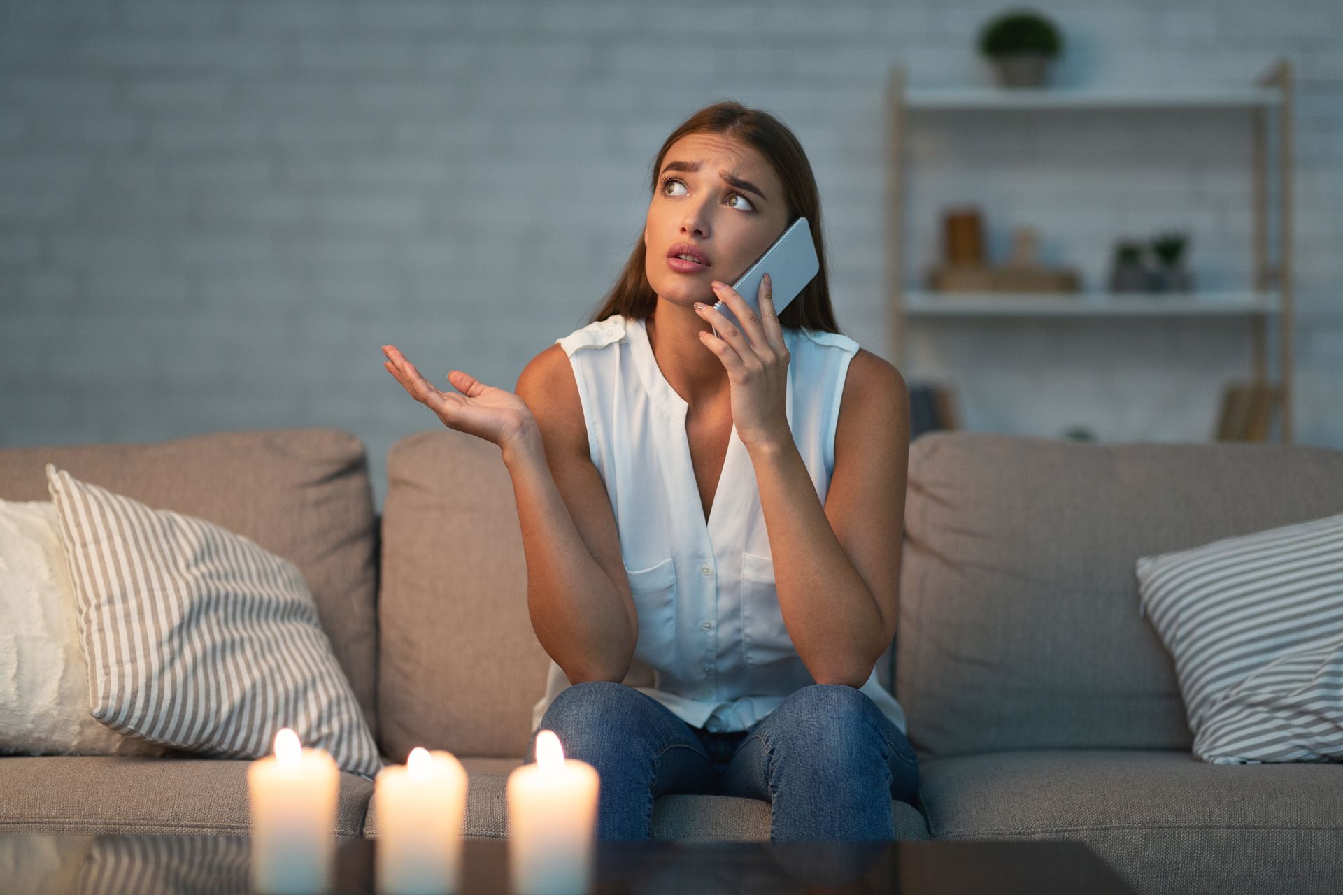 Woman on a couch speaking on the phone beside lit candles, looking concerned
