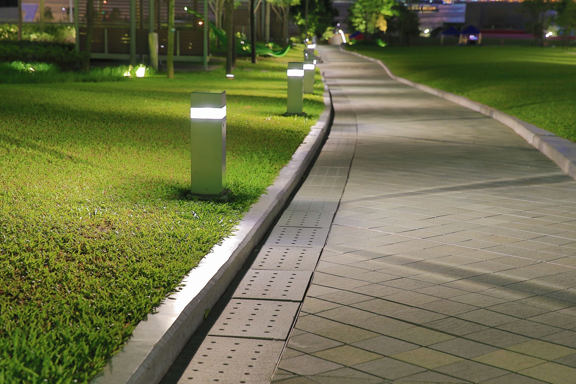 Curved illuminated walkway beside a grassy lawn at night with small path lights