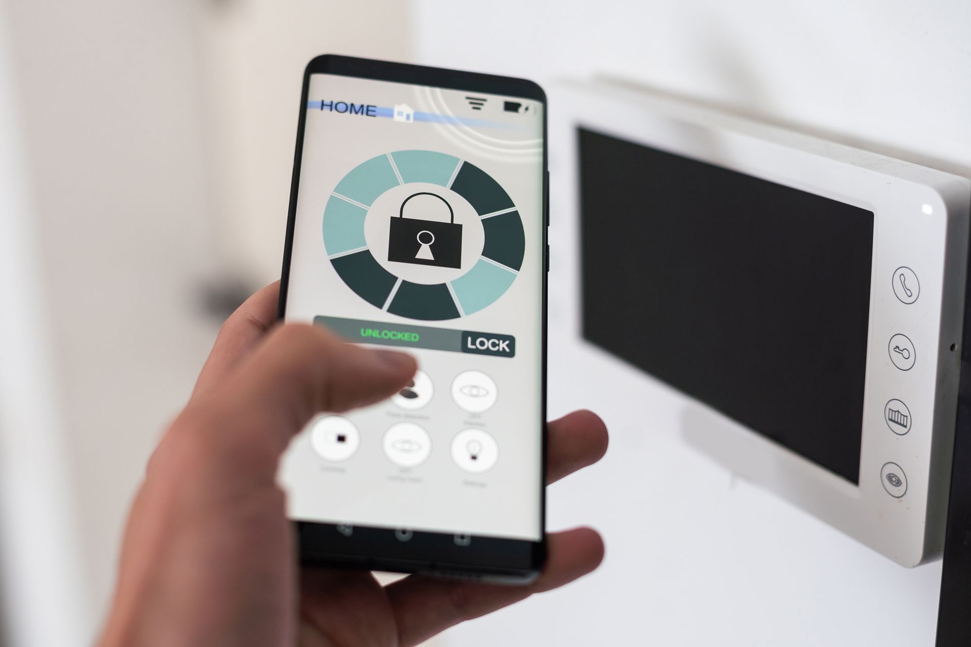 Hand holding smartphone controlling a wall-mounted video intercom with lock icon on screen