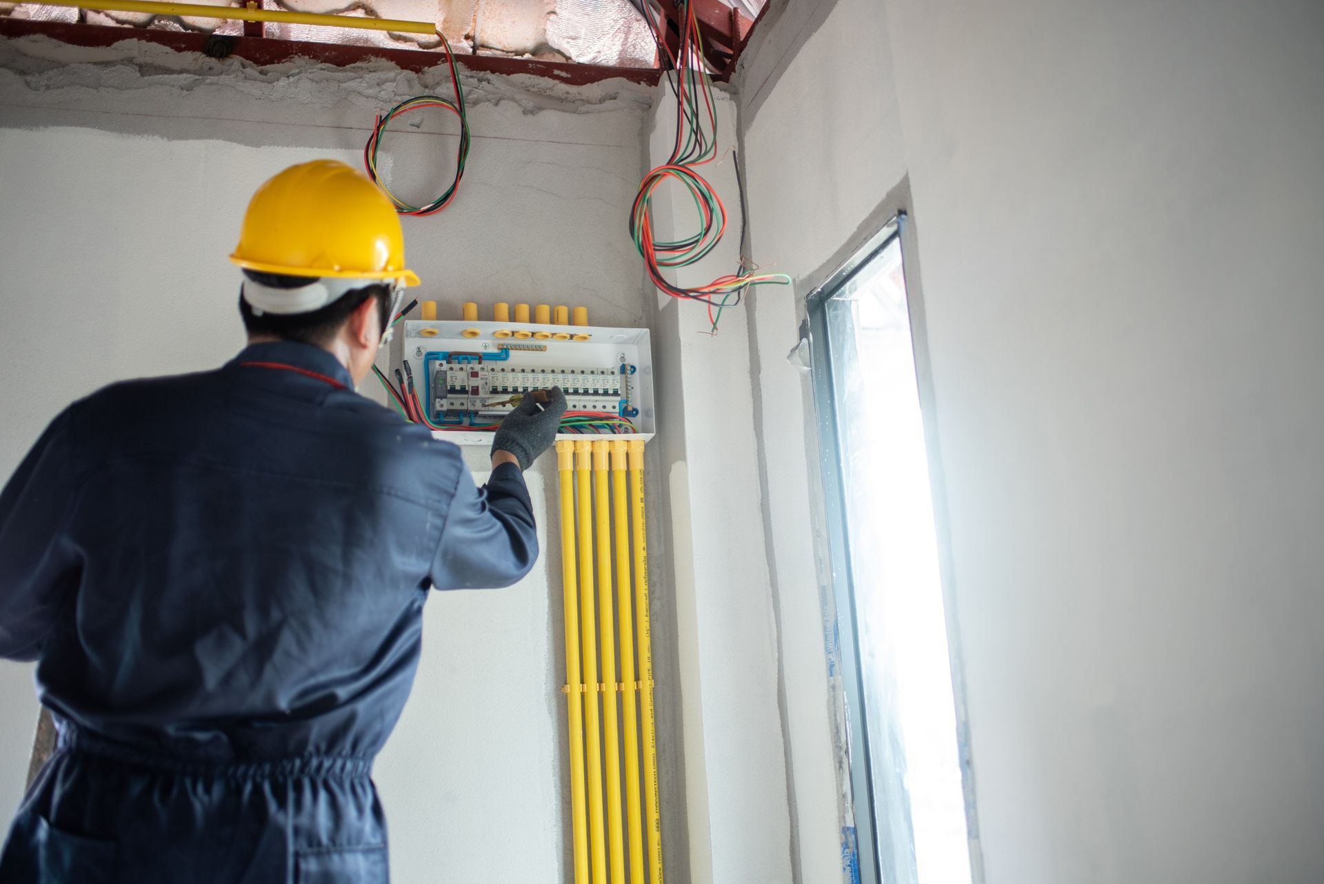 Electrician in a hard hat working on an electrical panel in a room under construction