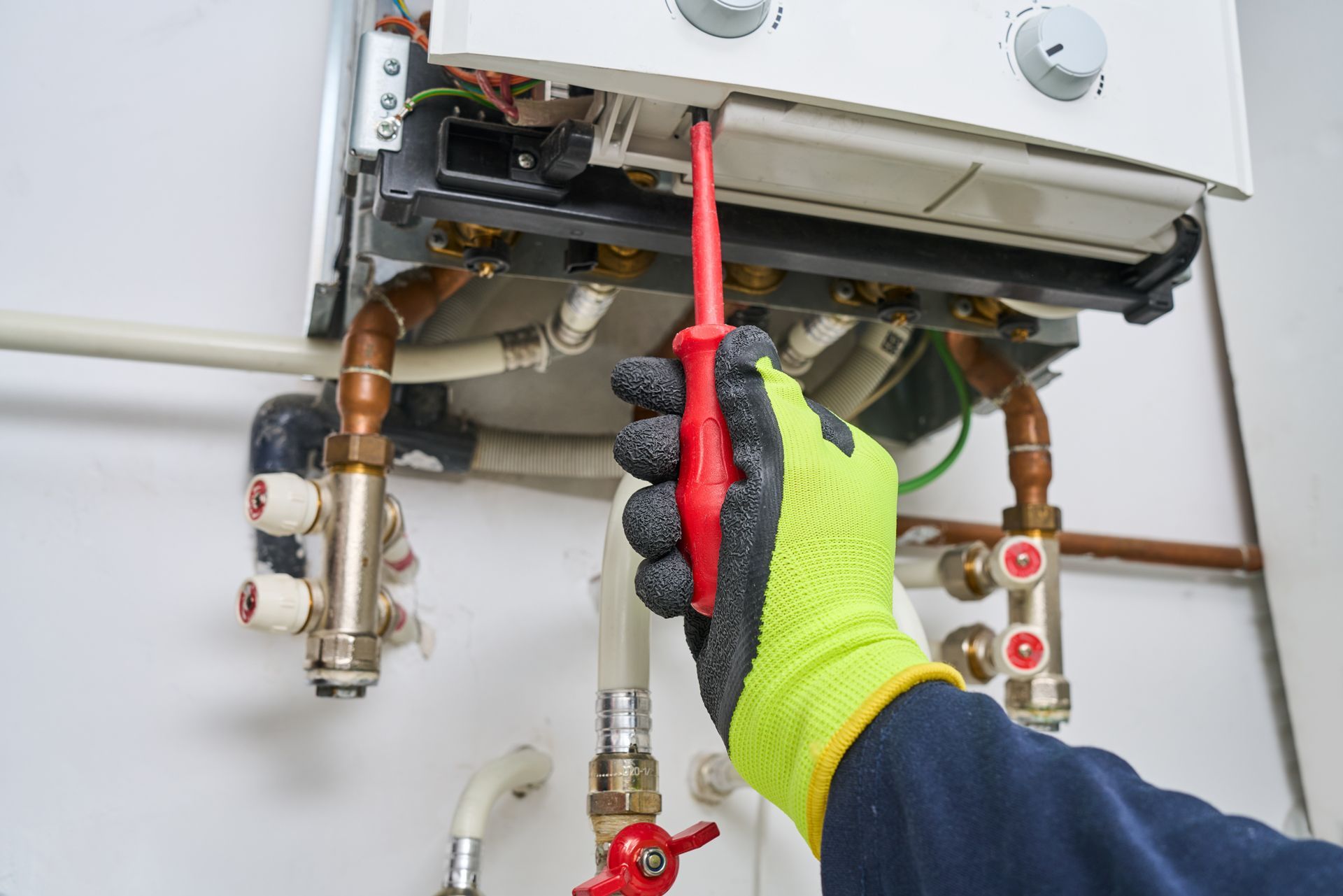 Technician testing a wall-mounted boiler with a red screwdriver and yellow glove
