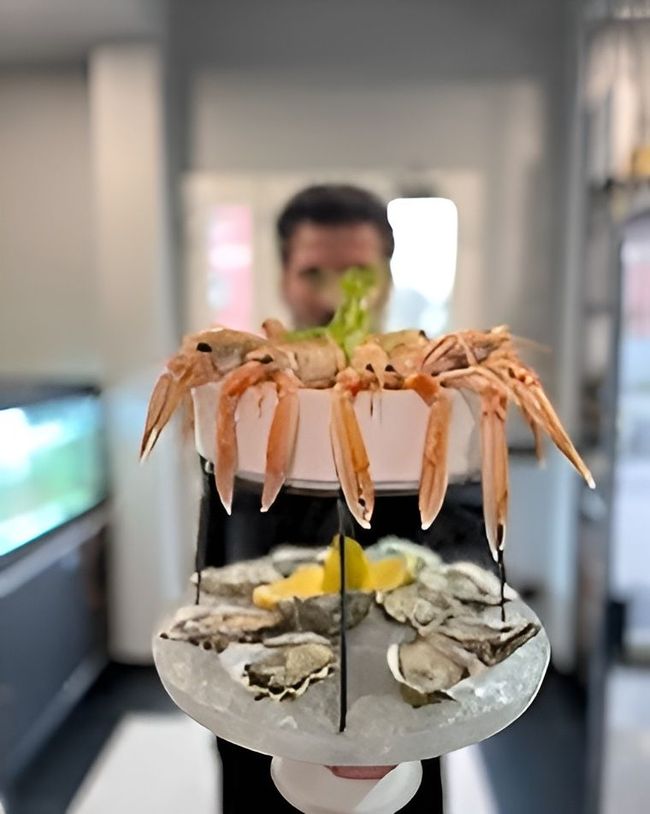 Piatto di frutti di mare con ostriche, limone e gamberi su un supporto in un ristorante; persona sfocata sullo sfondo.