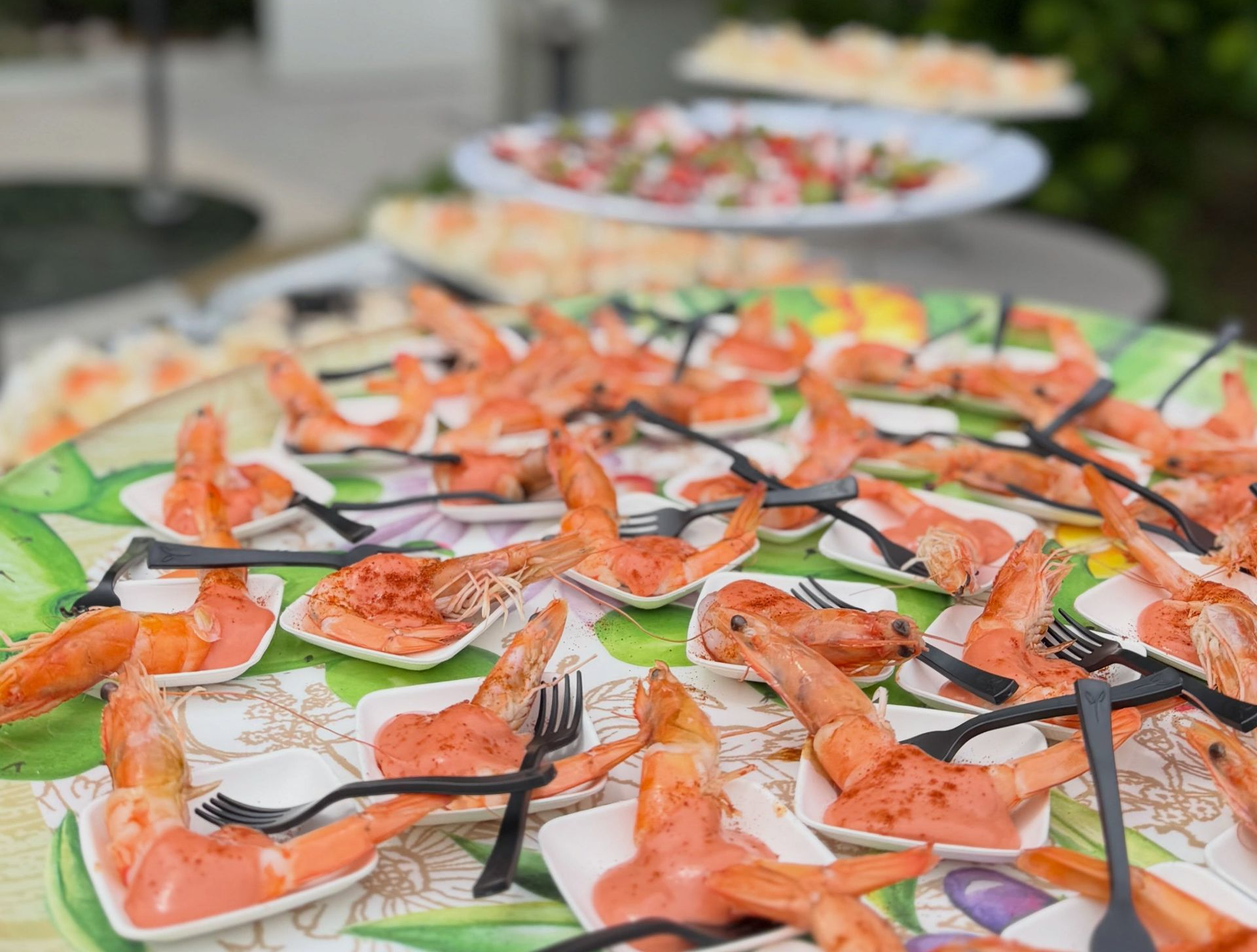 Piatti di gamberi e verdure disposti su un tavolo da buffet, con antipasti sullo sfondo.