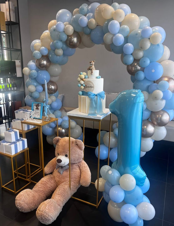 Allestimento per baby shower all'aperto con decorazioni blu e beige, torta, orsacchiotti e un arco sospeso vicino a un patio.