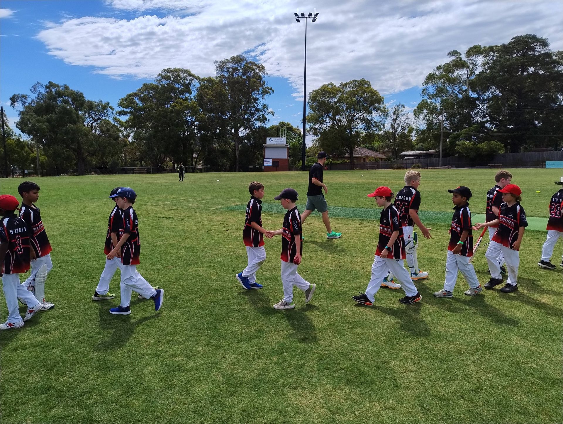 Children in BCC junior cricket uniforms walk across a grassy field shaking hands and congratulating each other.