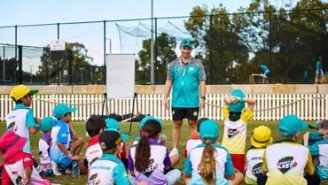 Coach speaking to a group of children seated outdoors before a Cricket Blast session.