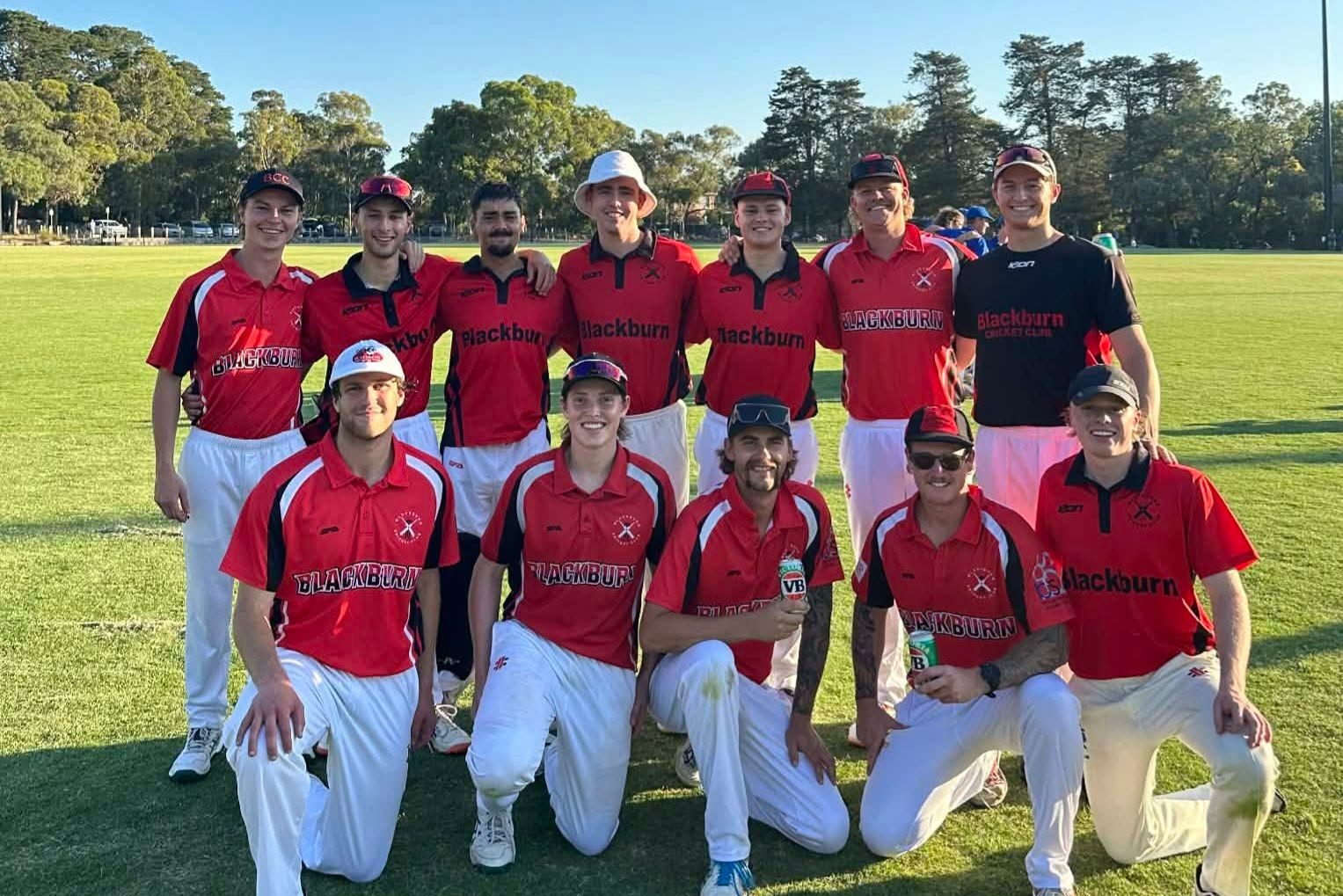 Social T20 team posing on a sunny field in red jerseys and white pants, celebrating the end of their season.