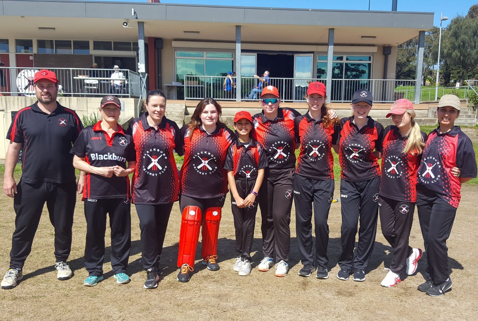 Social T20 team posing on a sunny field in red jerseys and white pants, celebrating the end of their season.