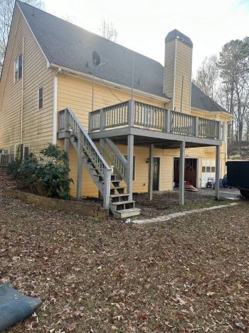 A large yellow house with a large deck and stairs.