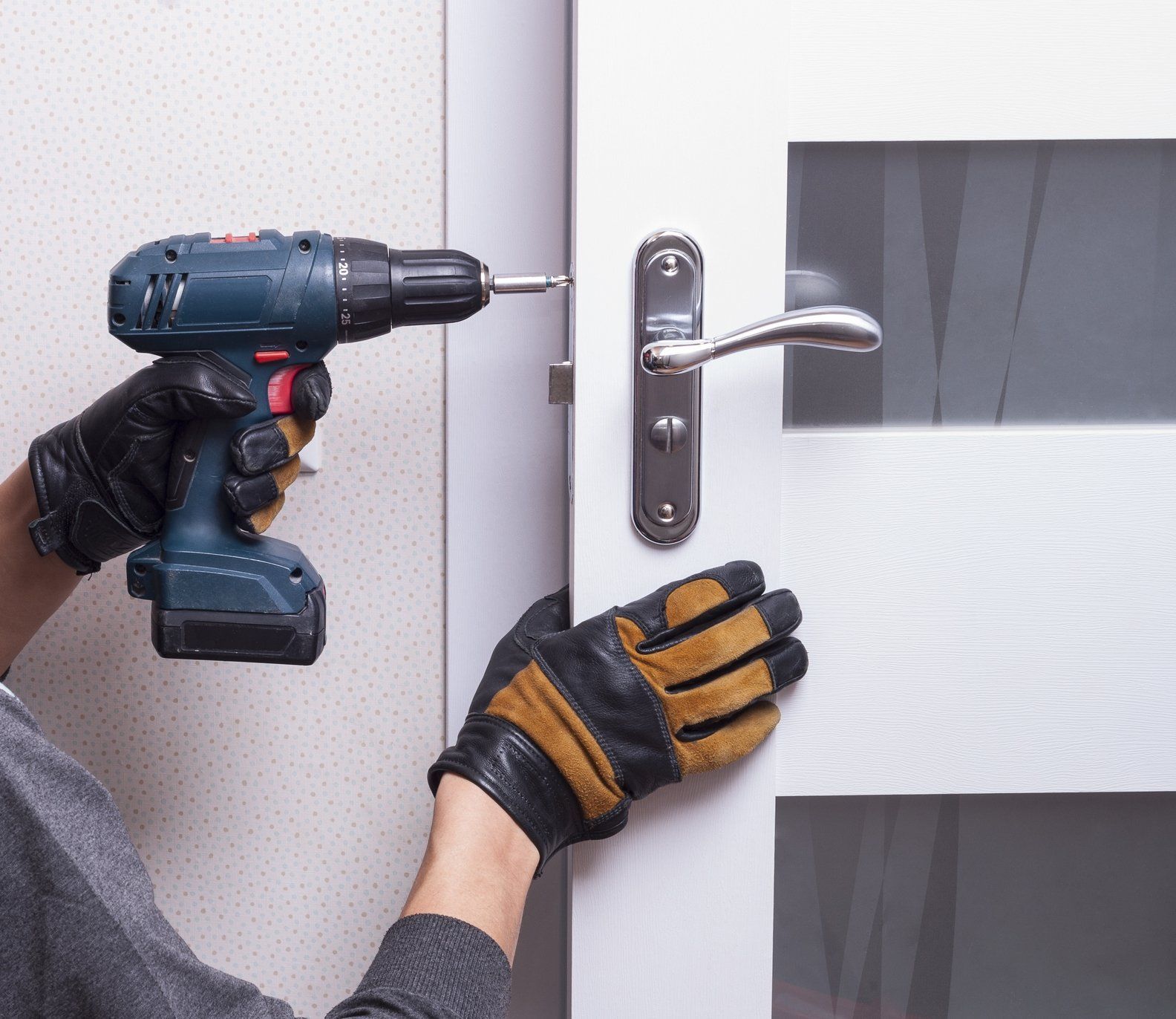 A person is using a drill to fix a door handle.