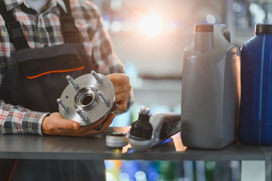 Mechanic holding a metal car part beside oil containers in a workshop