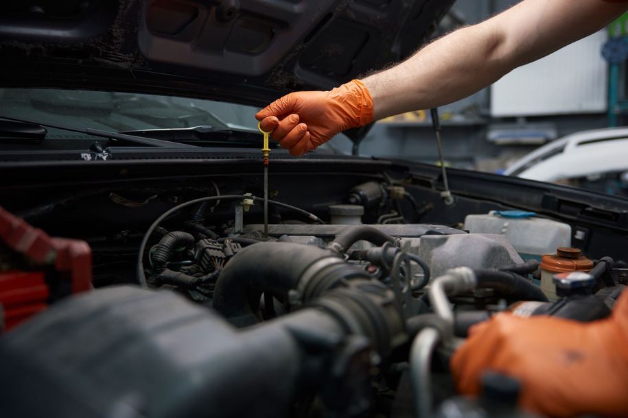 Mechanic in orange gloves checking oil under a car hood in a workshop