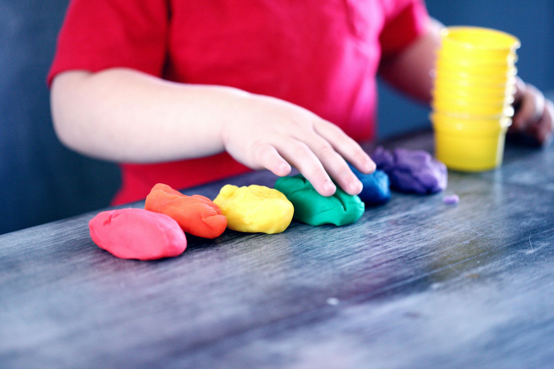 A child is playing with colorful play dough on a table.