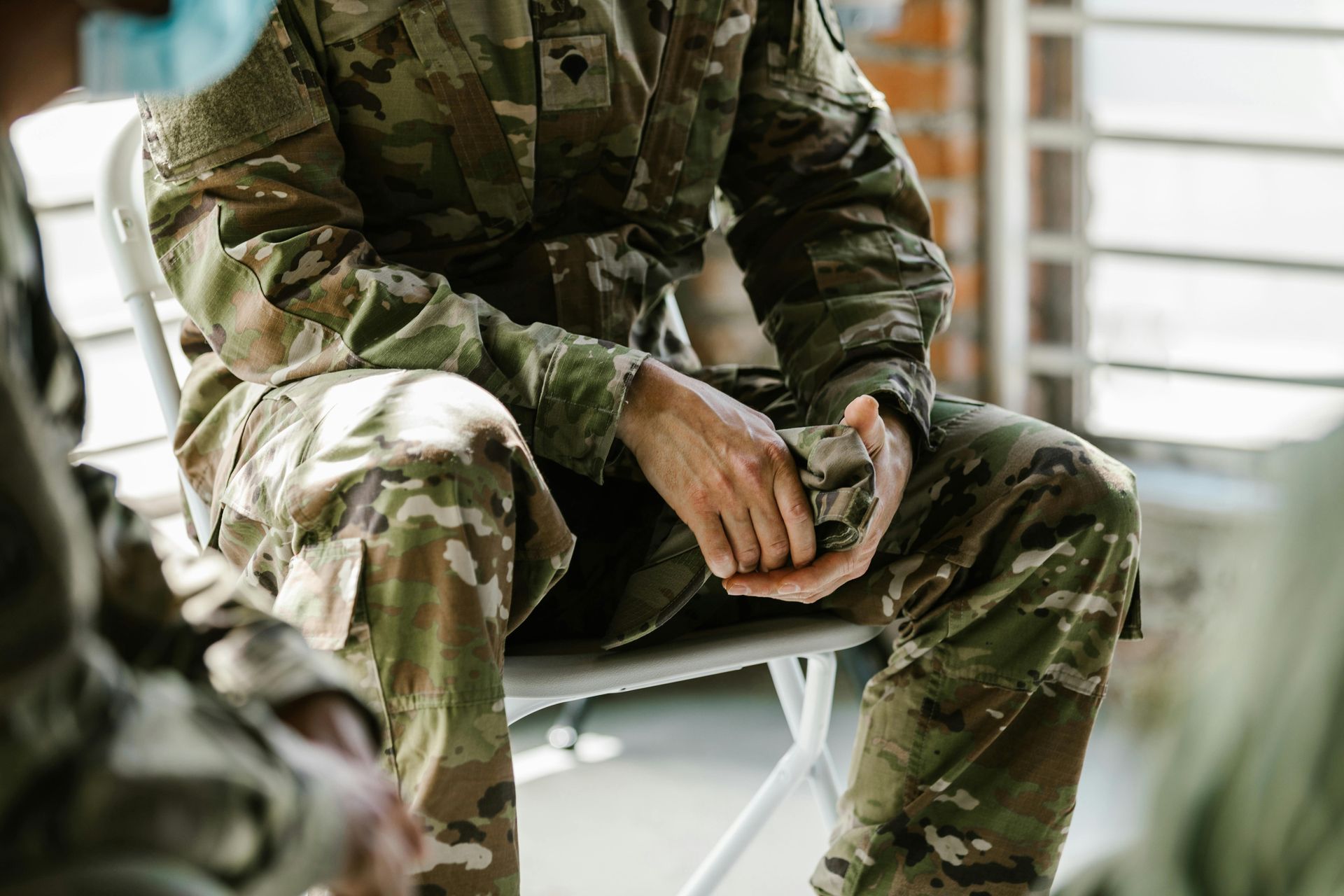 A soldier is sitting in a chair talking to another soldier.