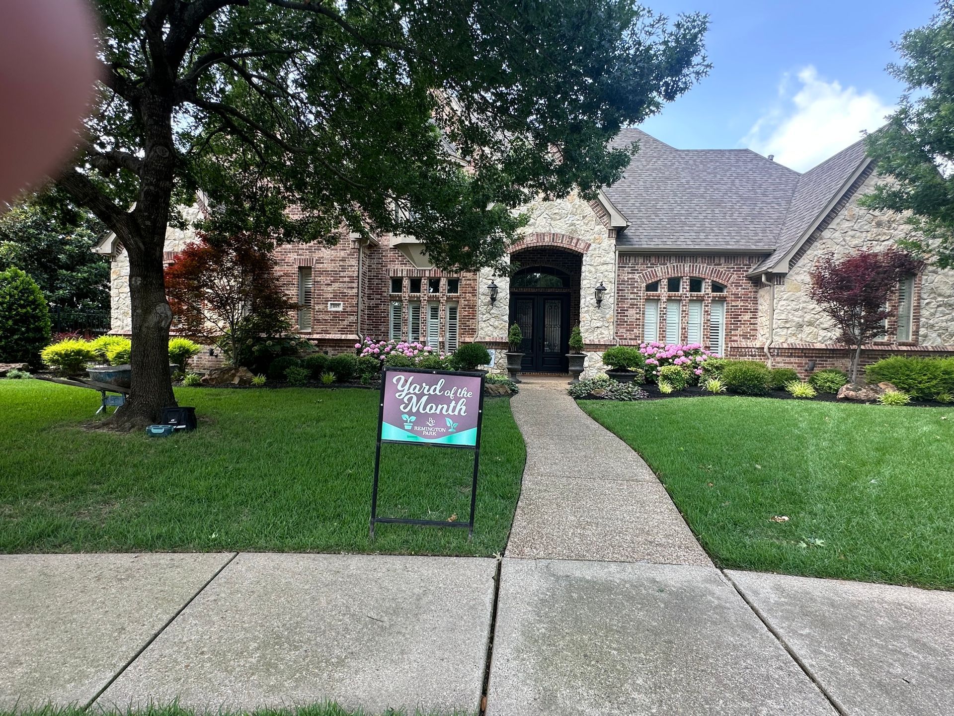 Brick Colleyville home with a front lawn, stone walkway, and a small yard sign by the entrance.