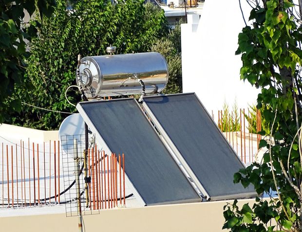 Uno scaldabagno solare in metallo con due pannelli collettori rettangolari scuri, montato su un tetto soleggiato.