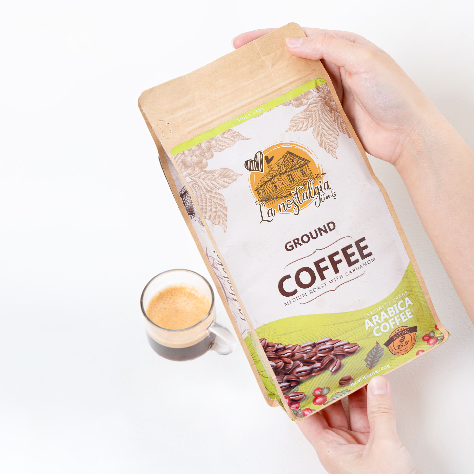 A person is holding a bag of ground coffee next to a cup of coffee.