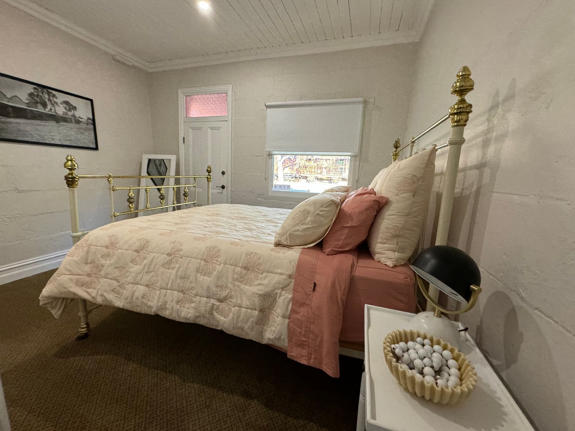 Bedroom with a bed, nightstand, and artwork on the wall. Neutral tones with touches of pink.