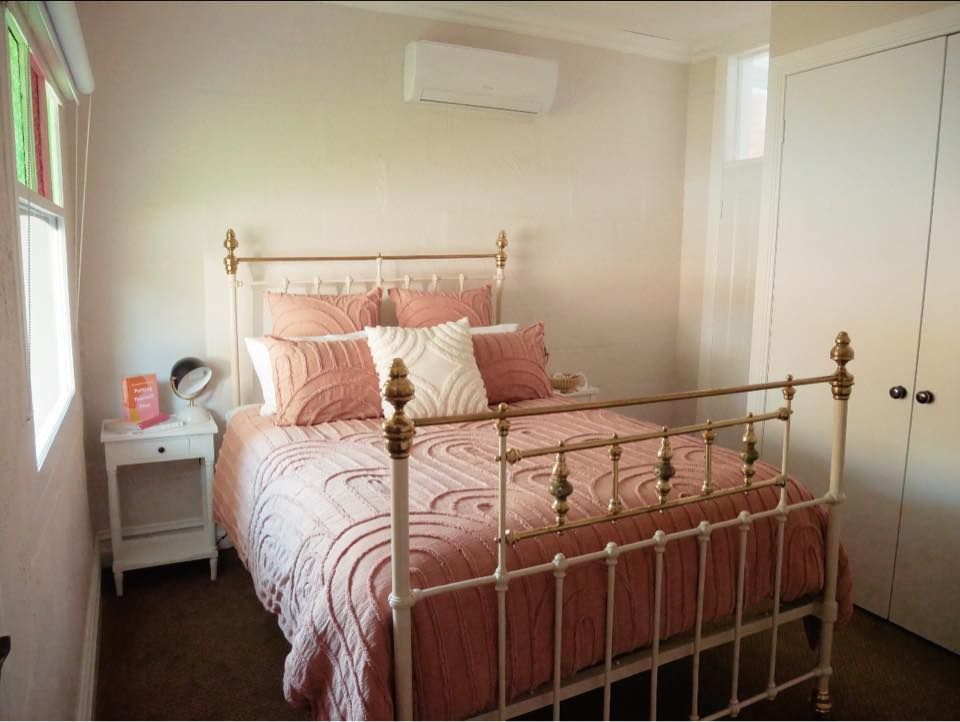 Bedroom with a white and gold bed frame, pink bedding, and a white nightstand.