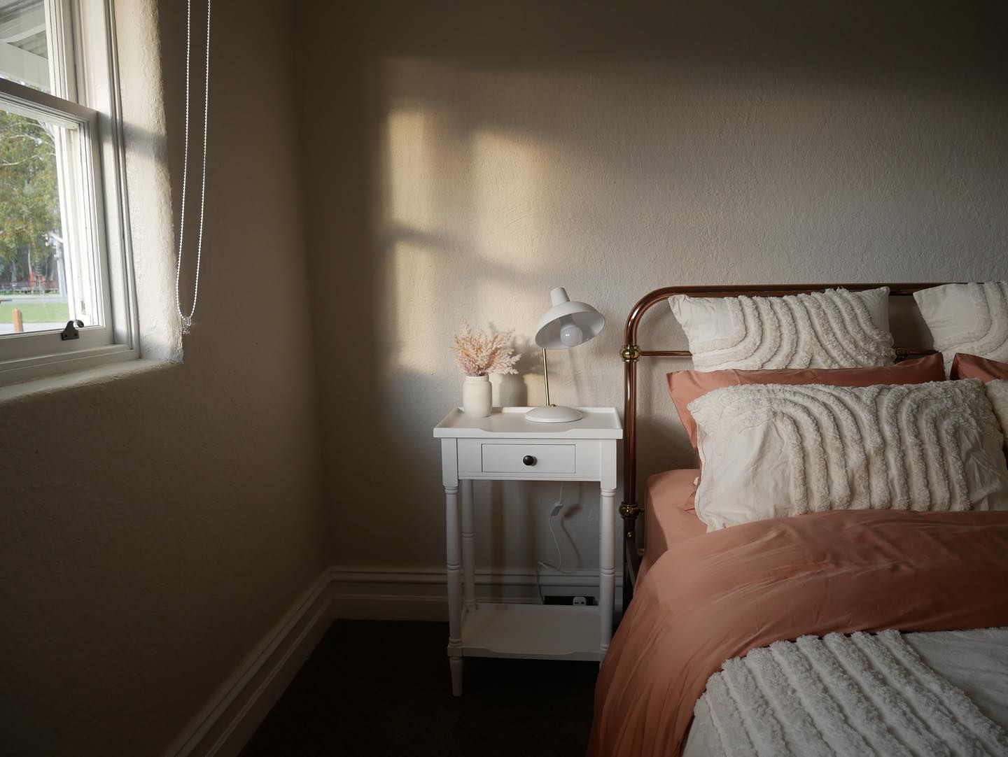 Bedroom interior with bed, nightstand, and window. Warm sunlight casts shadows.
