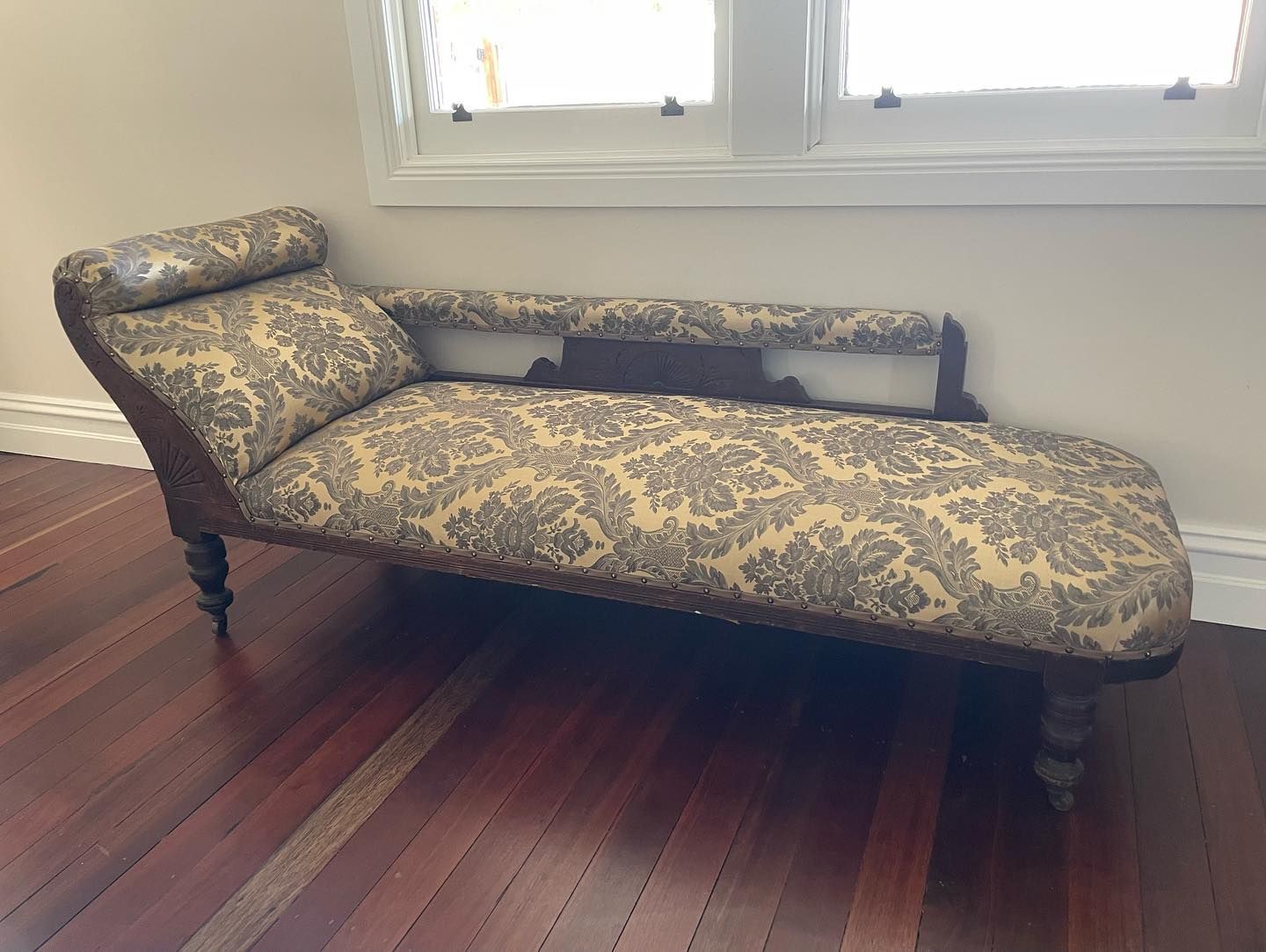 Chaise lounge with patterned gold and brown fabric. Dark wooden frame with ornate detailing.