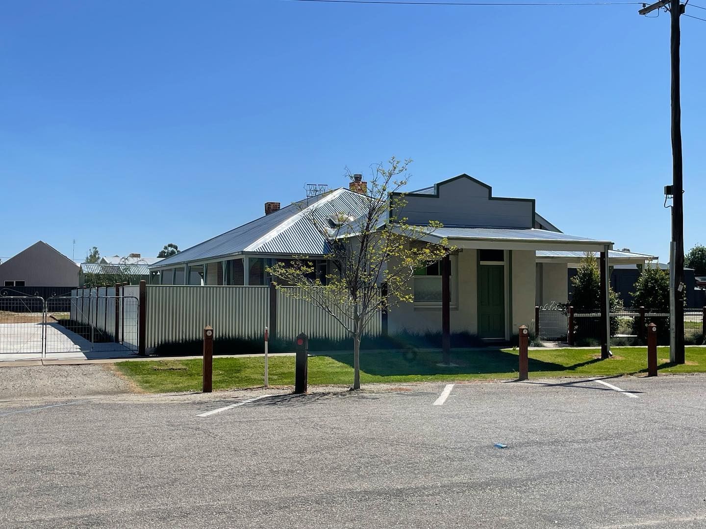 A light-colored building with a corrugated iron roof, next to a white picket fence on a sunny day.