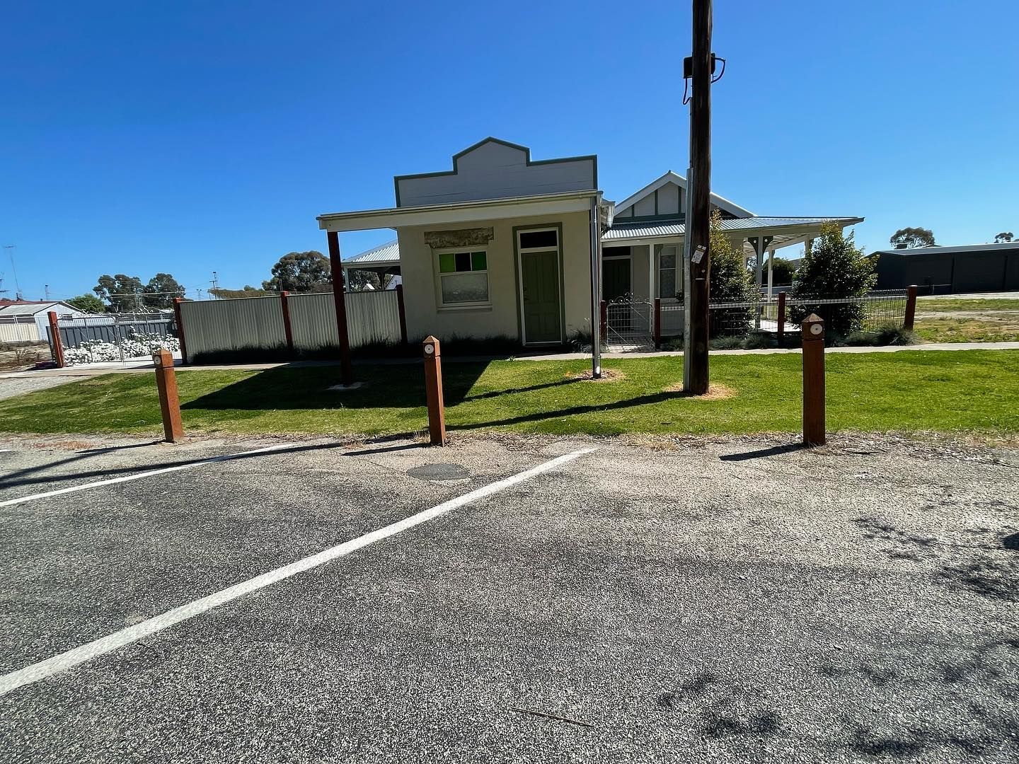 Small white building with green door and awning, in a gravel parking lot on a sunny day.