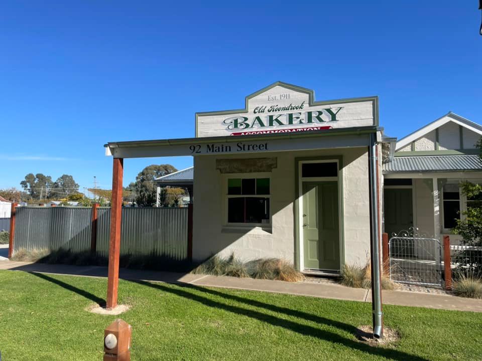 Old-fashioned bakery, painted in cream and green, with a sign above the door that reads “Old Established Bakery” and “12 Main Street.