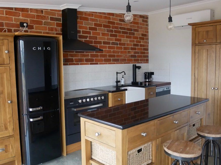 Black and brick kitchen with island, appliances, and light wood cabinets.