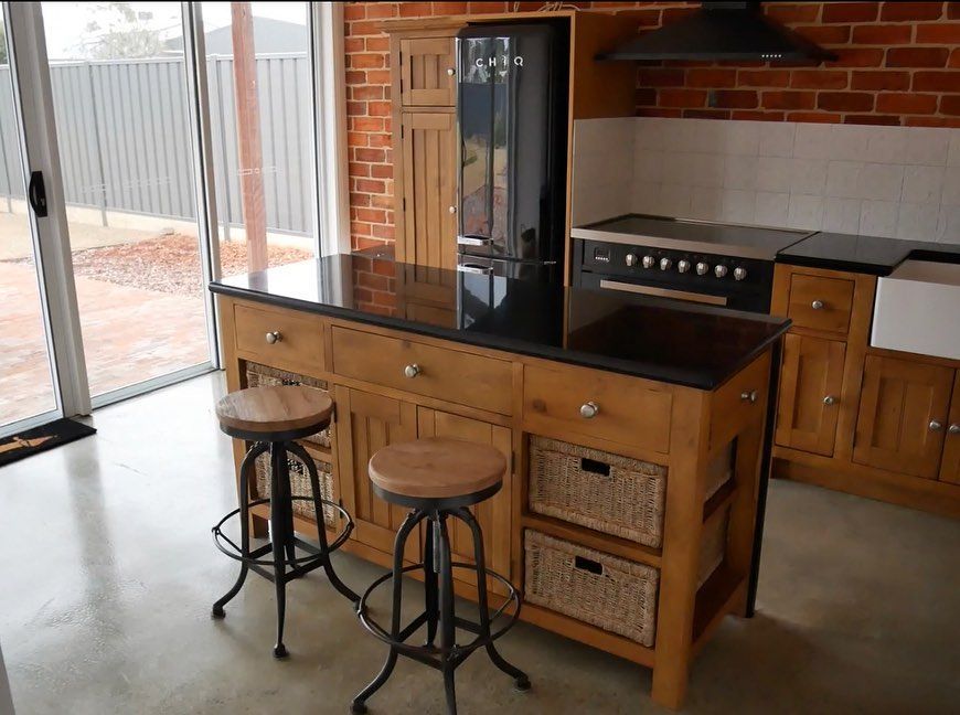 Kitchen with wooden island, black countertops, stools, brick wall, and black appliances.