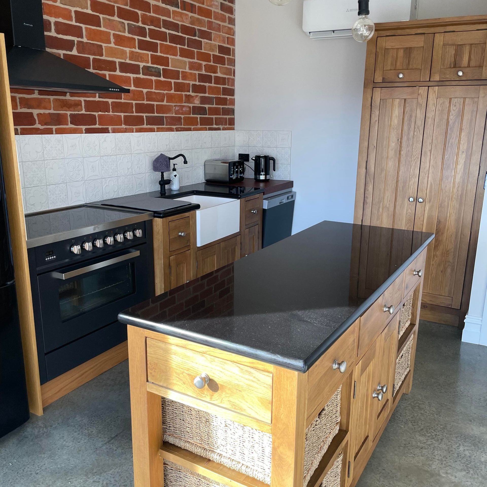 Kitchen with brick wall, oak cabinets, black countertops, island, stove, and sink.