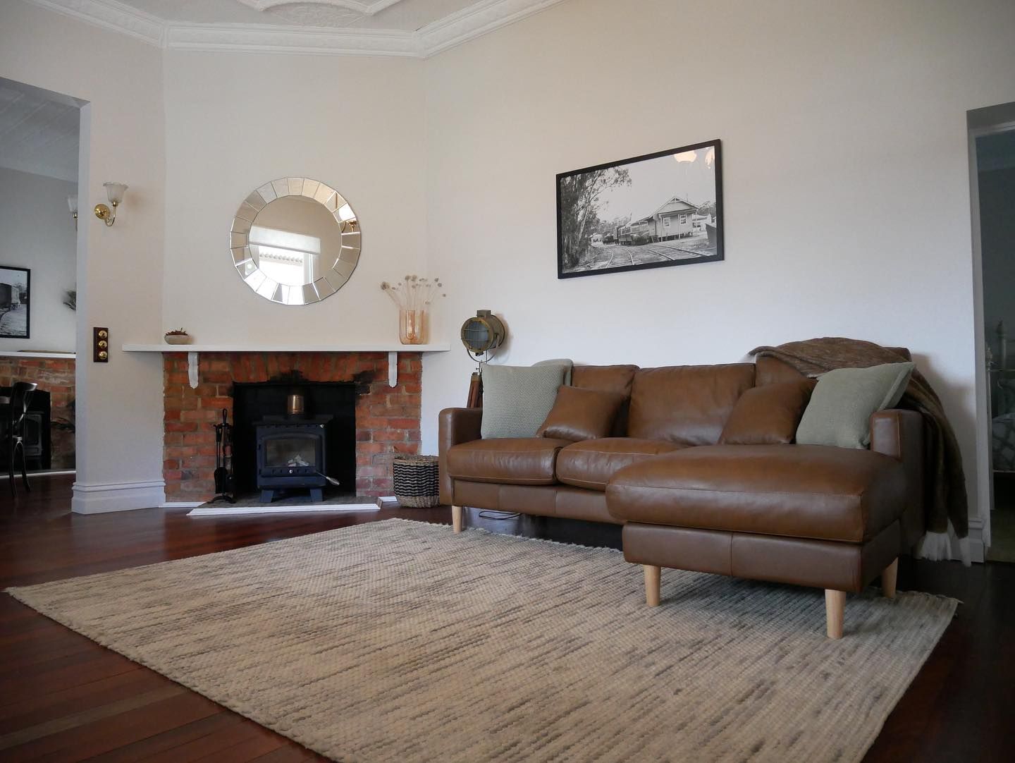 Living room with brown leather sectional, fireplace, mirror, and light-colored rug.