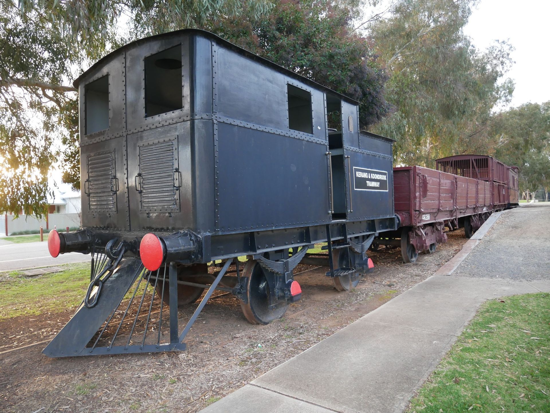 Black train and two red boxcars on a track in a park.