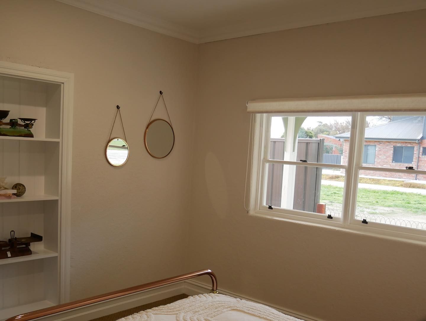 Bedroom with mirrors, window, built-in shelves, and a bed with copper accents. Beige walls and white trim.