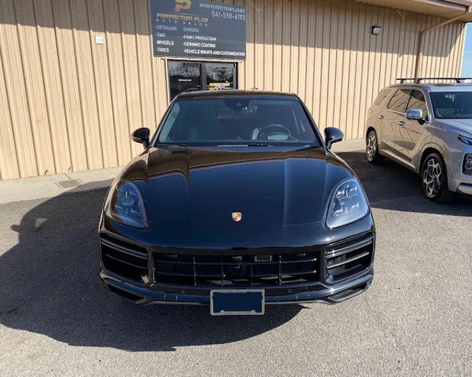 Black Porsche Cayenne with front PPF coverage, parked outside Perfection Plus Auto Salon shop