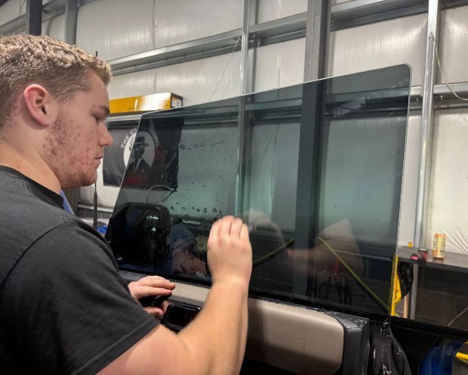 Technician smoothing tinted windows film on van glass during installation