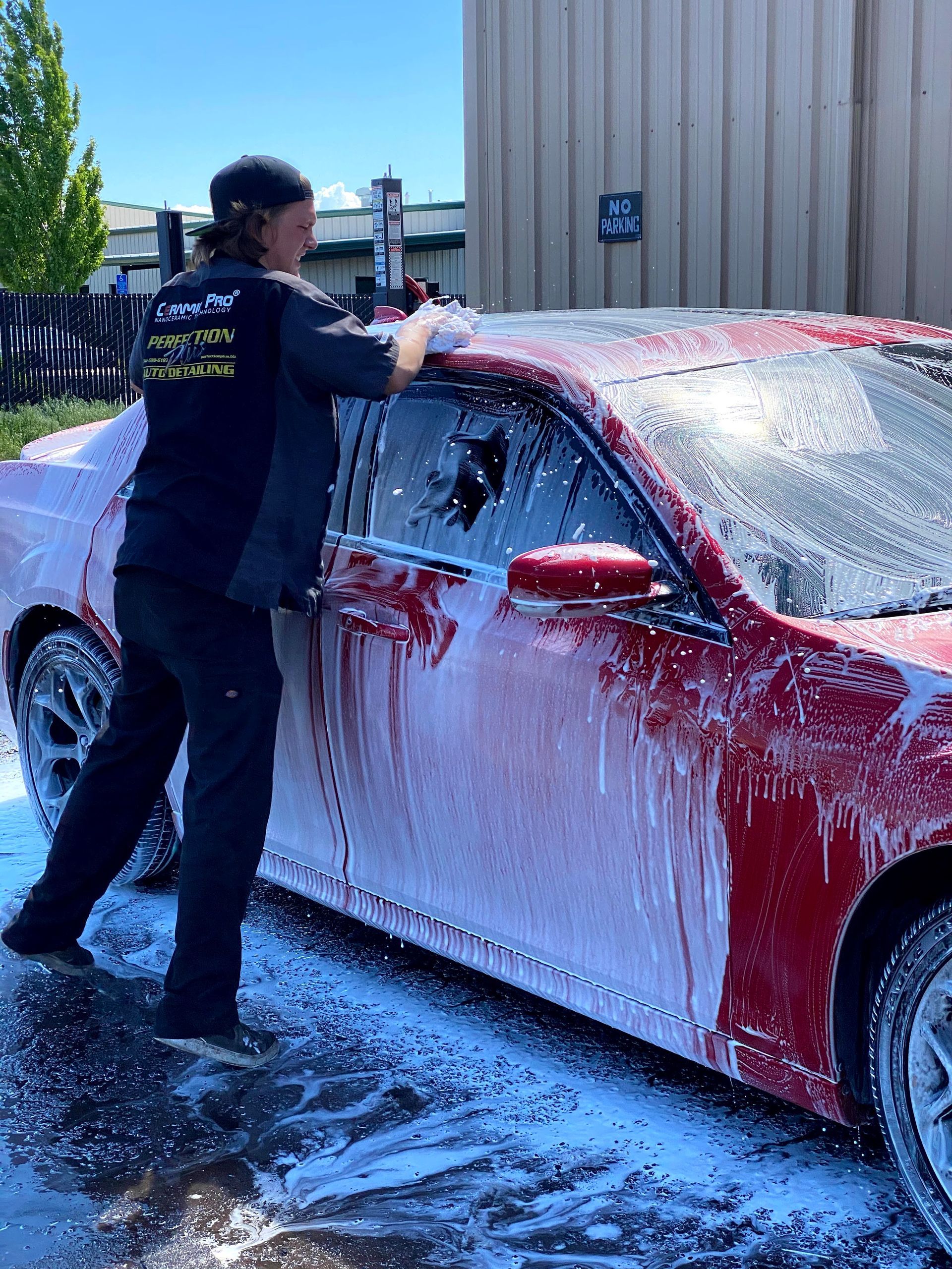 Man washing a red car with thick soap foam outdoors in bright sunlight