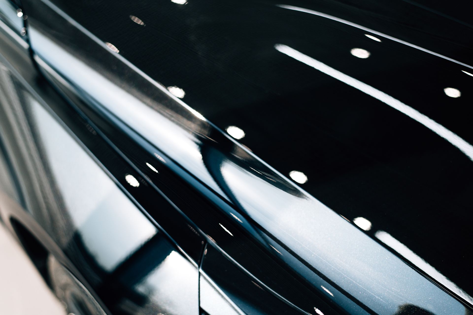 Close-up of a glossy black car roof with reflections and overhead lights