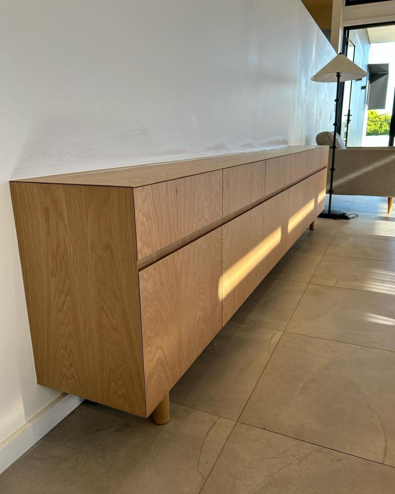 A Long Wooden Cabinet is Sitting on a Tiled Floor in a Living Room — Precision Kitchens & Cabinets in Ballina, NSW