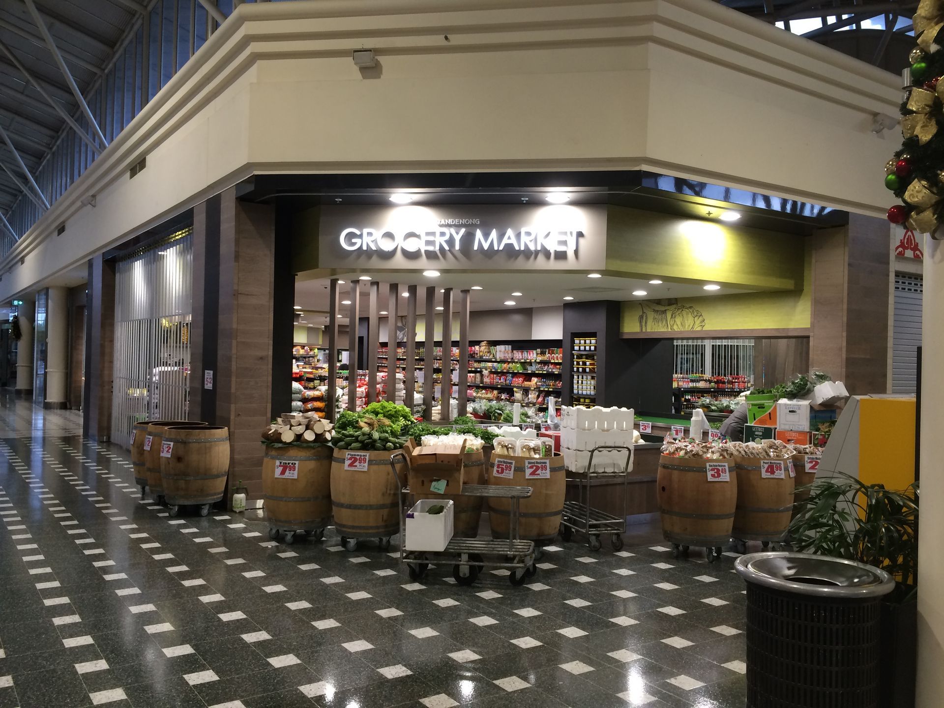 Gourmet market storefront with flower buckets and produce displays inside a tiled shopping arcade