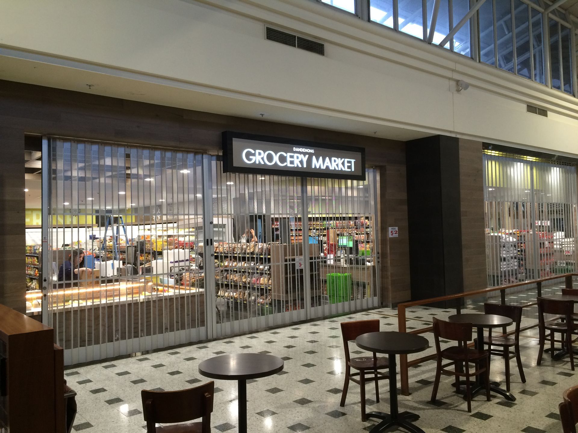Indoor shopping corridor with a grocery market storefront and tables in the foreground