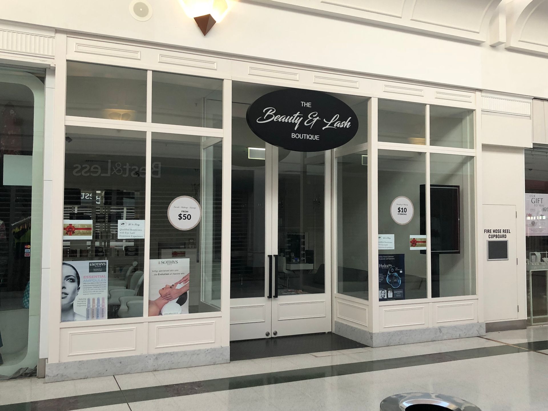 Storefront with large windows and a black oval sign above the entrance in a shopping mall corridor