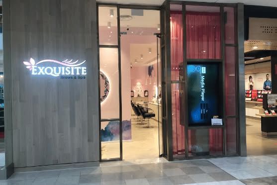 Storefront entrance with glowing “EXQUISITE” sign, glass doors, and a lit display case inside.
